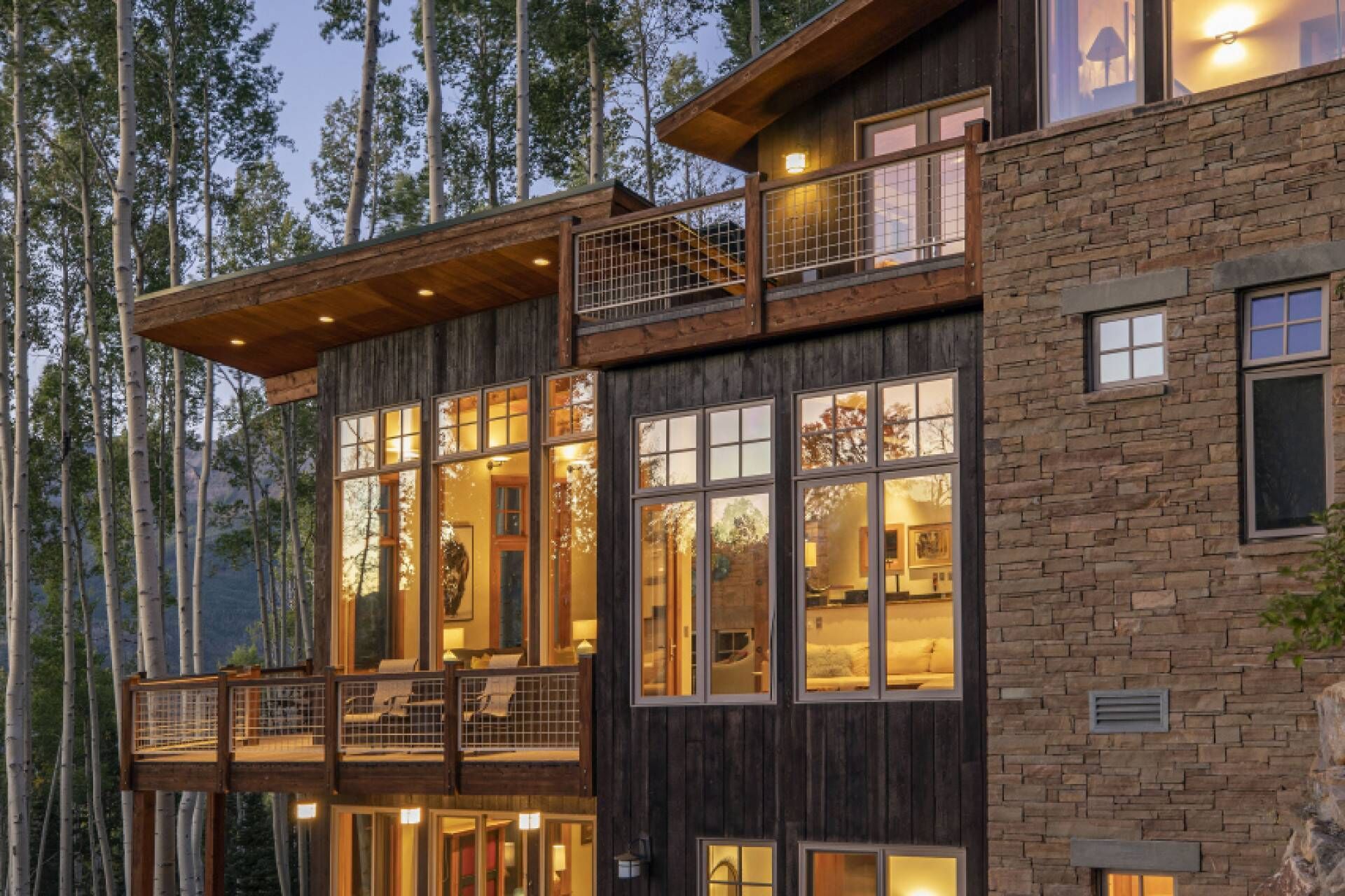 A multi-story log cabin with large windows, a balcony, and a stone facade.