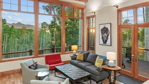 A spacious living room with large windows, a sofa, chairs, and a coffee table. - Canyon View Retreat - Scenic & Secluded (Telluride)