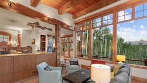 A spacious living area with a large window offering a view of trees and mountains. There is a wooden ceiling, a dining area, and a kitchen with wooden cabinets. - Canyon View Retreat - Scenic & Secluded (Telluride)