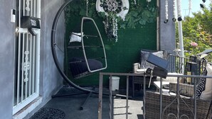 Un espacio al aire libre cubierto con un sillón colgante, una mesa con sillas y una pared decorada con luces y plantas colgantes.