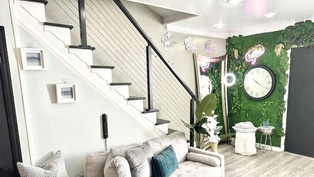 Una sala de estar moderna con una escalera, un sofá y una pared verde con plantas.