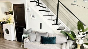 Una sala de estar con un sofá gris, una lavadora, una escalera y una planta.