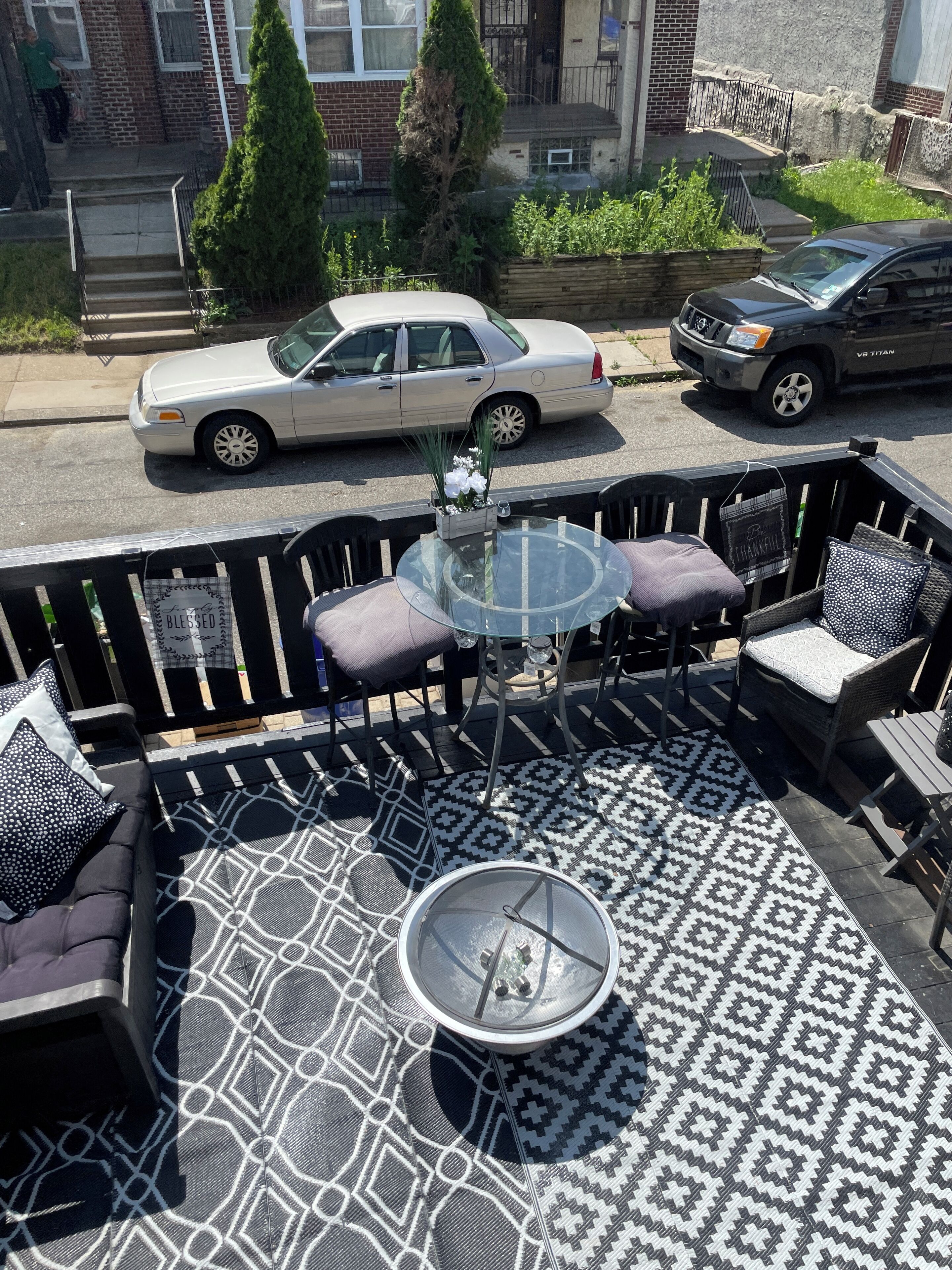 Une terrasse extérieure avec une table en verre, entourée de sièges confortables et agrémentée d’un tapis à motifs.