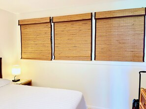 A hotel room with a bed, a nightstand with a lamp, and a wall-mounted panel with a bamboo-like texture. - Gorgeous Oceanfront Unit at Kona Isle! Ground Floor! Greatly Updated! (Kailua-Kona)