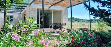 Una casa moderna con un porche cubierto, un comedor y un jardín con plantas en flor.
