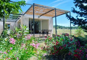 Una casa moderna con portico coperto, zona pranzo e giardino fiorito.