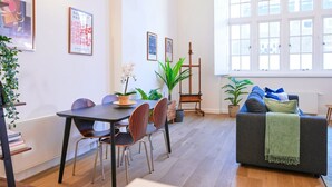 Uma sala de estar moderna com área de jantar, destacando uma mesa de madeira, cadeiras, um sofá e diversas plantas.