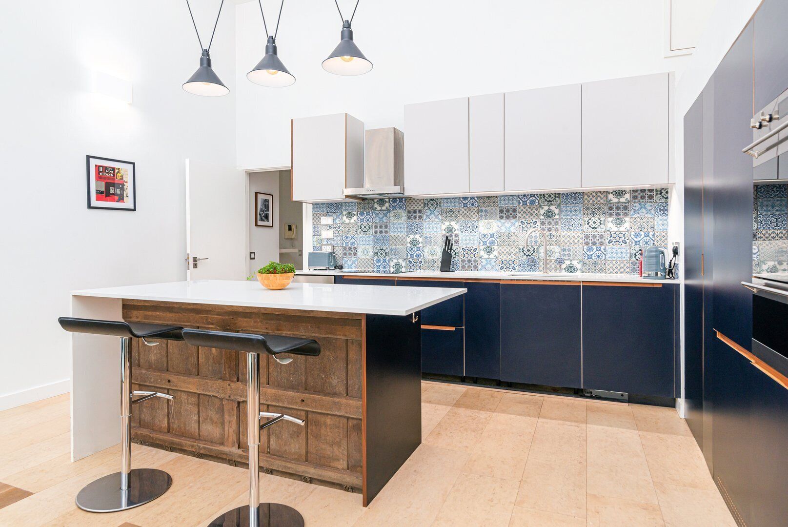 Une cuisine moderne dotée d’un îlot central, de tabourets de bar, de luminaires suspendus et d’un revêtement mural en carreaux.