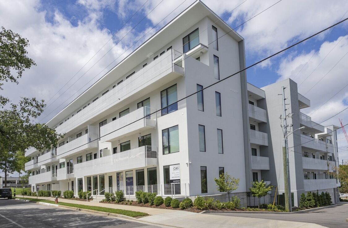 A modern multi-story building with balconies, a parking lot, and a clear sky.