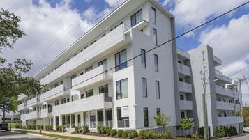 A modern multi-story building with balconies, a parking lot, and a clear sky.