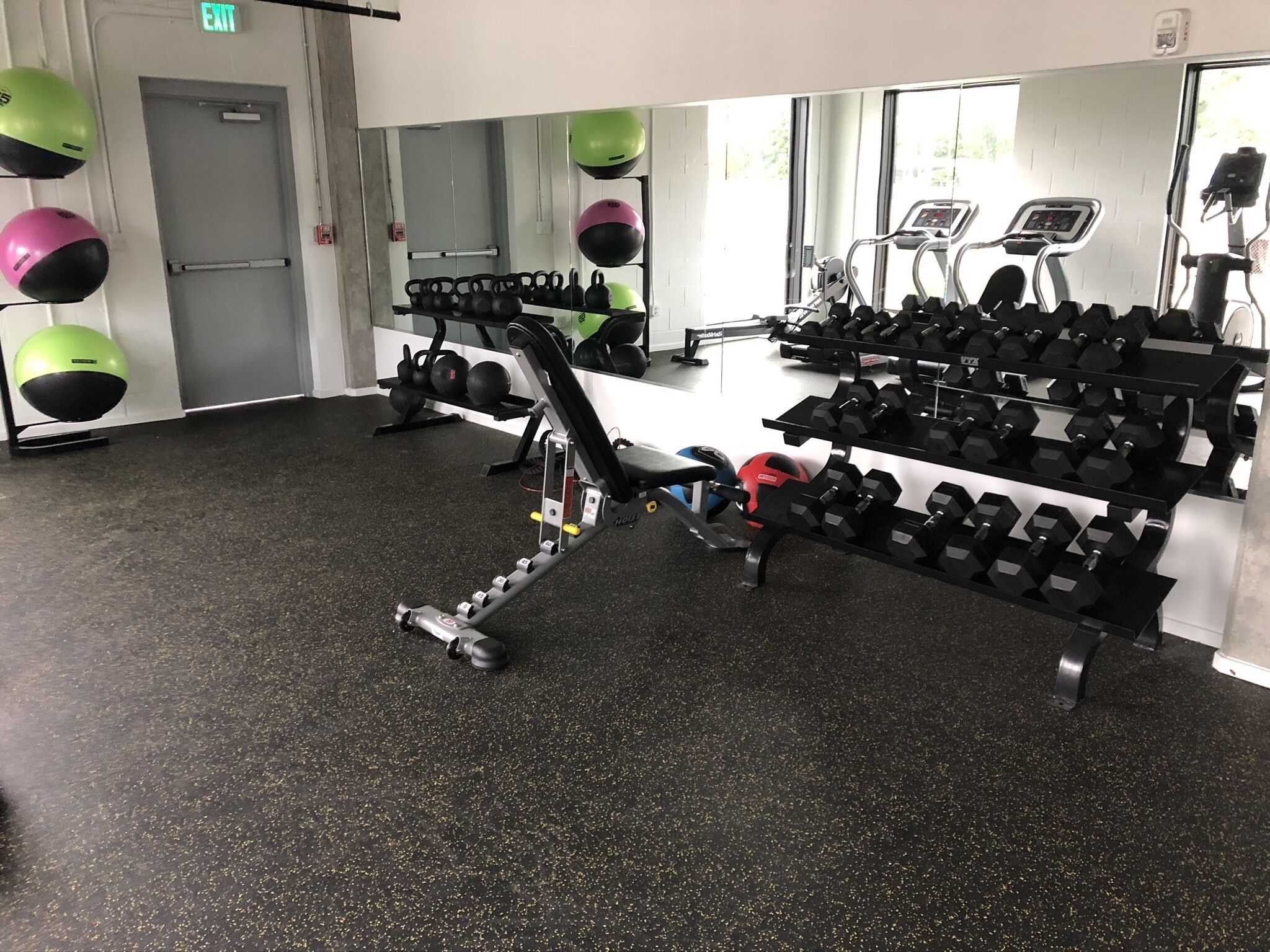 A gym with exercise equipment, including kettlebells, dumbbells, and a bench.