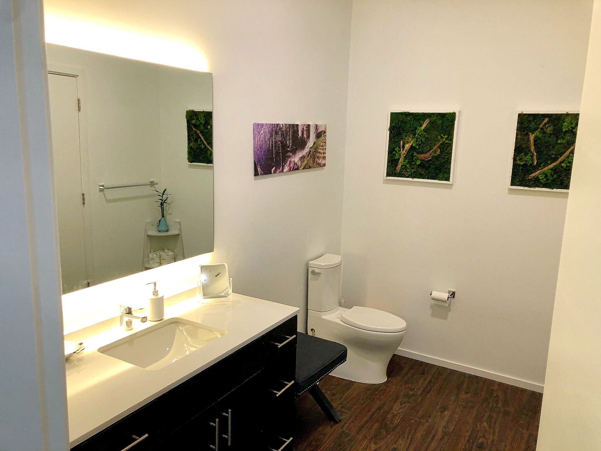Un baño moderno con un lavamanos blanco, tocador negro y un inodoro blanco. Hay tres cuadros en la pared.