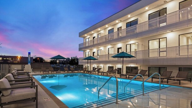 A modern hotel with a swimming pool, sun loungers, and a covered area with umbrellas.