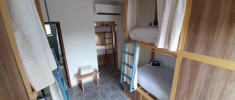 Et lille rum med køjesenge, et lille bord, en stige og en aircondition.