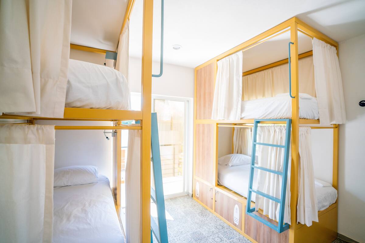 Ein Schlafsaalzimmer mit Stockbetten, einer Hängetreppe und Vorhängen.