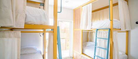 Un dormitorio tipo residencia con literas, una escalera y cortinas.