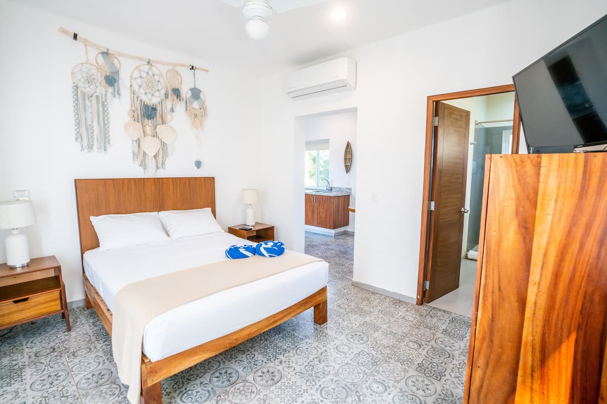Ein Schlafzimmer mit einem hölzernen Bett, einem Nachttisch, einem an der Wand befestigten Fernseher und einer Tür zu einem Badezimmer.