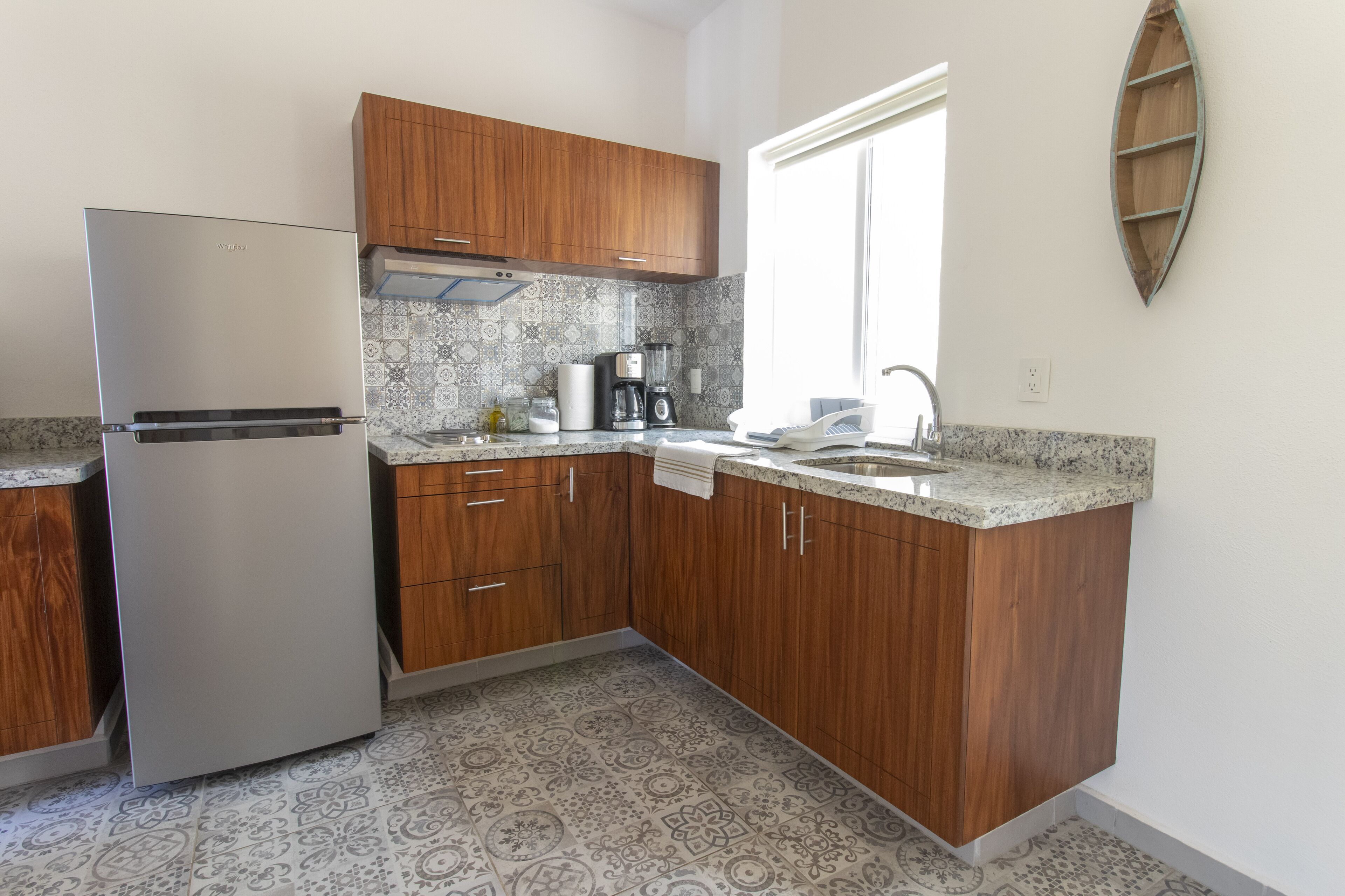 A kitchen with wooden cabinets, a stainless steel refrigerator, a coffee maker, and a patterned backsplash.