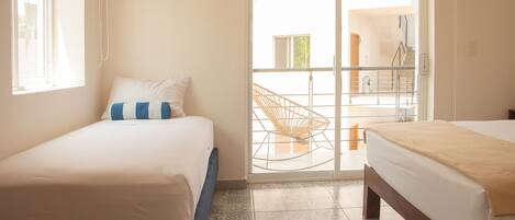 Una habitación con dos camas, un ventanal y una puerta corrediza de vidrio que da a un espacio exterior con una silla y una escalera.