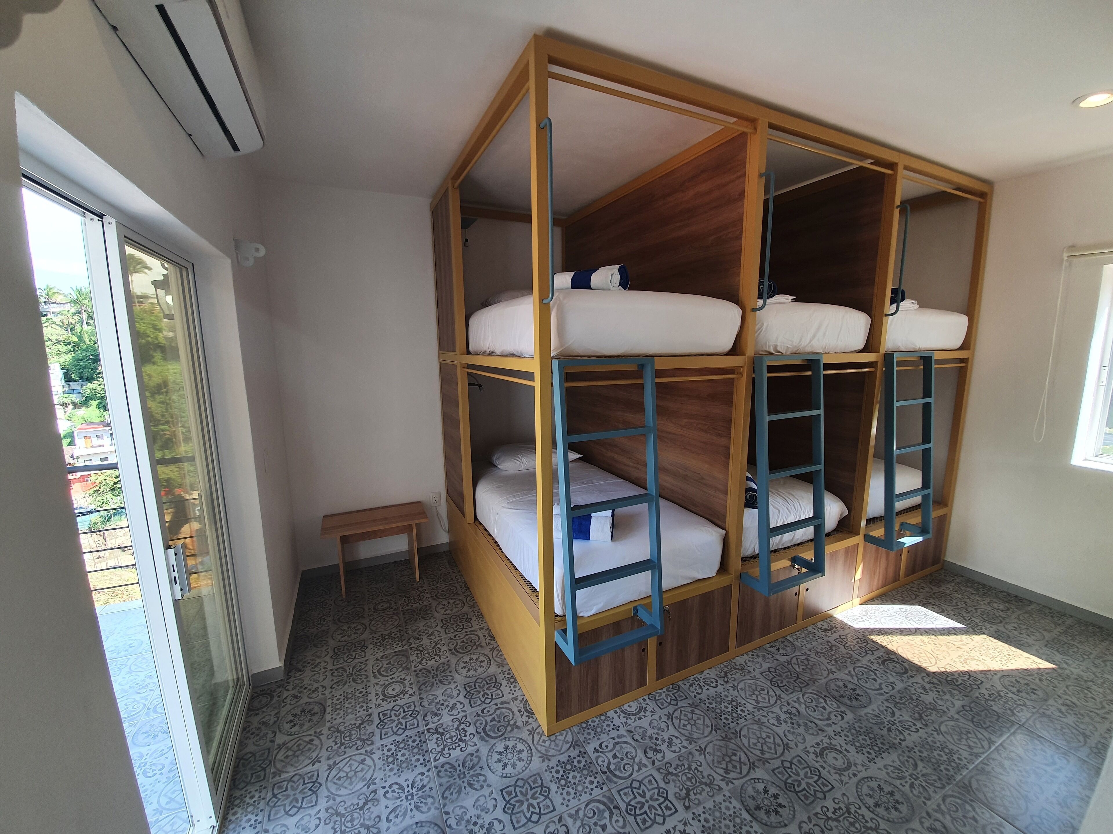 A room with a bunk bed, a small table, patterned floor tiles, and a window.