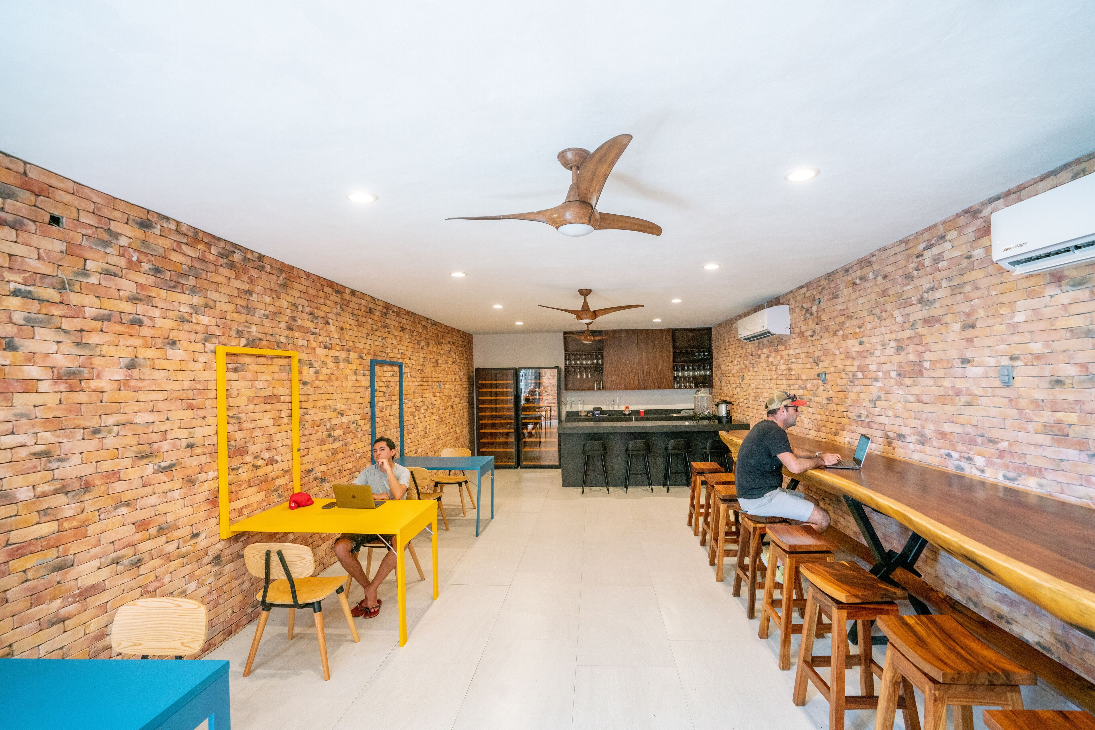 A spacious room with a brick wall, a yellow table, wooden chairs, and a long wooden bench.