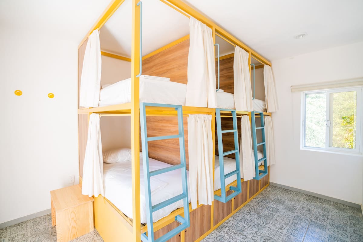 Ein Schlafraum mit Etagenbett, Fenster, Holzboden und einem kleinen Holzschemel.