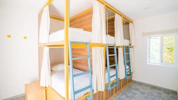 A bunk bed room with a window, wooden flooring, and a small wooden stool.