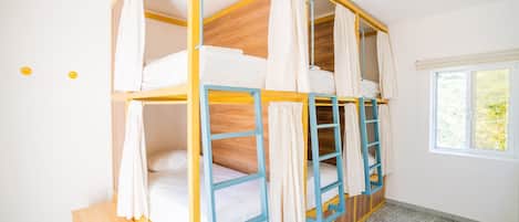 Dormitorio con literas, ventana, suelo de madera y un taburete pequeño de madera.