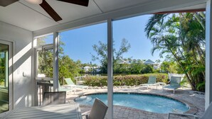 A pool area with a table and chairs, surrounded by a patio with a view of a residential neighborhood and a body of water.