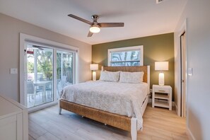 Ein Schlafzimmer mit einem Bett, einem Deckenventilator, einem Nachttisch mit Lampe und einer Schiebetür zu einem Außenbereich.