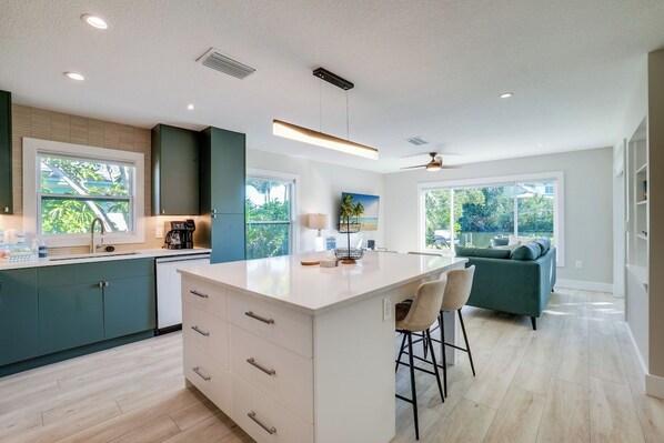 A modern kitchen with a central island, bar stools, and a view of the outdoors.