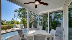 A covered outdoor area with a pool, seating, and palm trees.