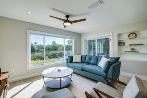 Ein geräumiges Wohnzimmer mit großem Fenster, Deckenventilator, blauem Sofa und rundem Couchtisch.