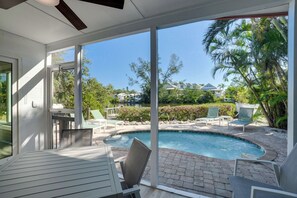 A pool area with a table and chairs, surrounded by a patio with a view of a residential neighborhood.