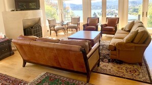 A spacious living room with leather sofas, a coffee table, and a fireplace. Large windows offer a view of a lake and mountains. - Take in the San Francisco views at this quiet oasis! (Tiburon)