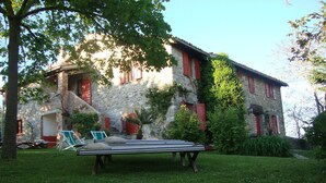 A stone building with red shutters, a grassy lawn, and a lounge chair.