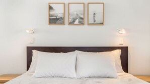 A bed with white linens, a dark headboard, and three framed photographs above it.