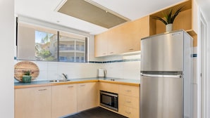 A modern kitchen with wooden cabinets, a stainless steel refrigerator, a built-in microwave, and a window with a view of a building.