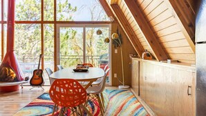 Ein gemütliches Zimmer mit Holzbalkendecke, einem runden Tisch mit Stühlen, einer Gitarre und einem farbenfrohen Teppich.