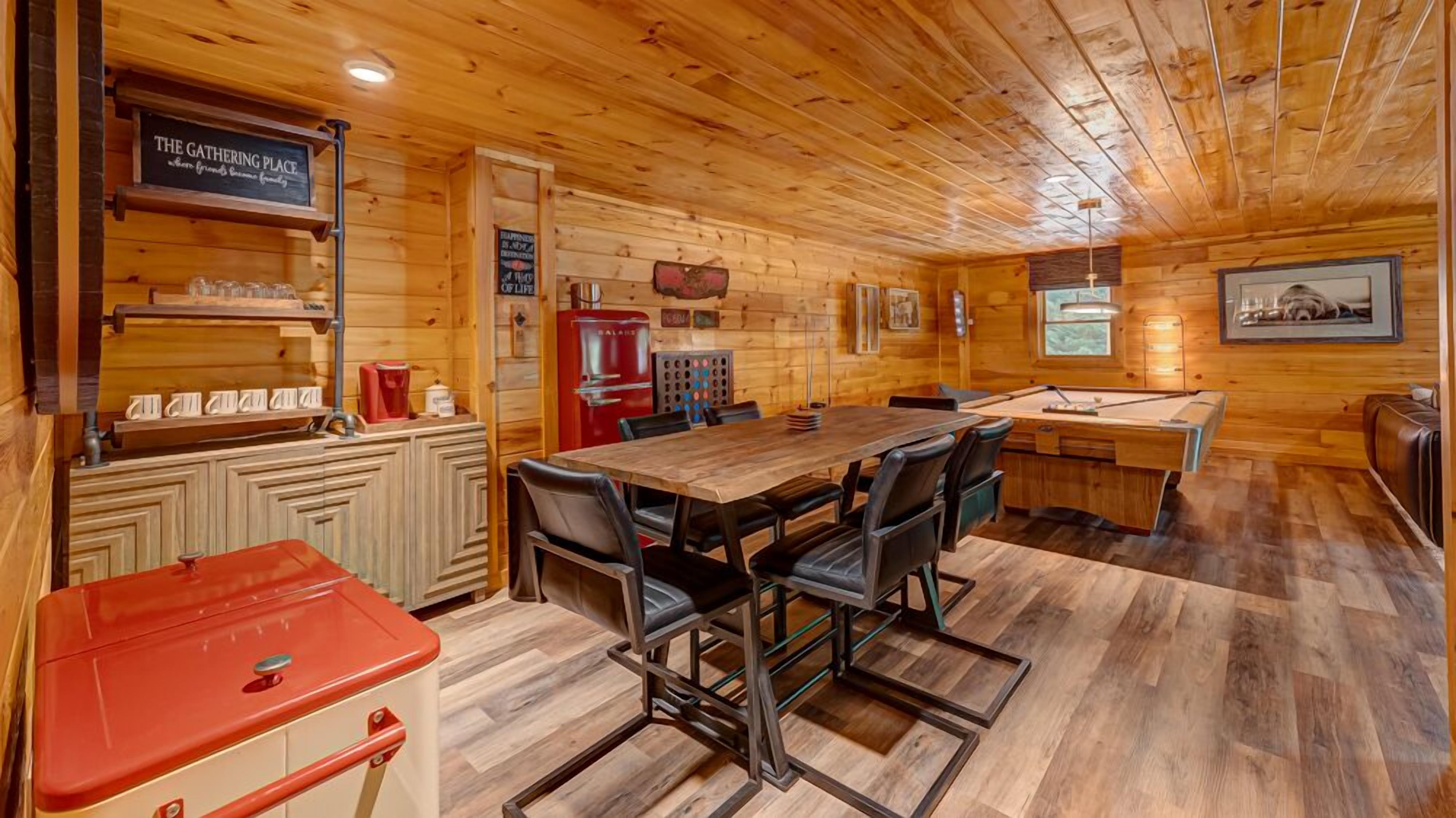 A wooden cabin interior with a dining area, a pool table, and a red grill.