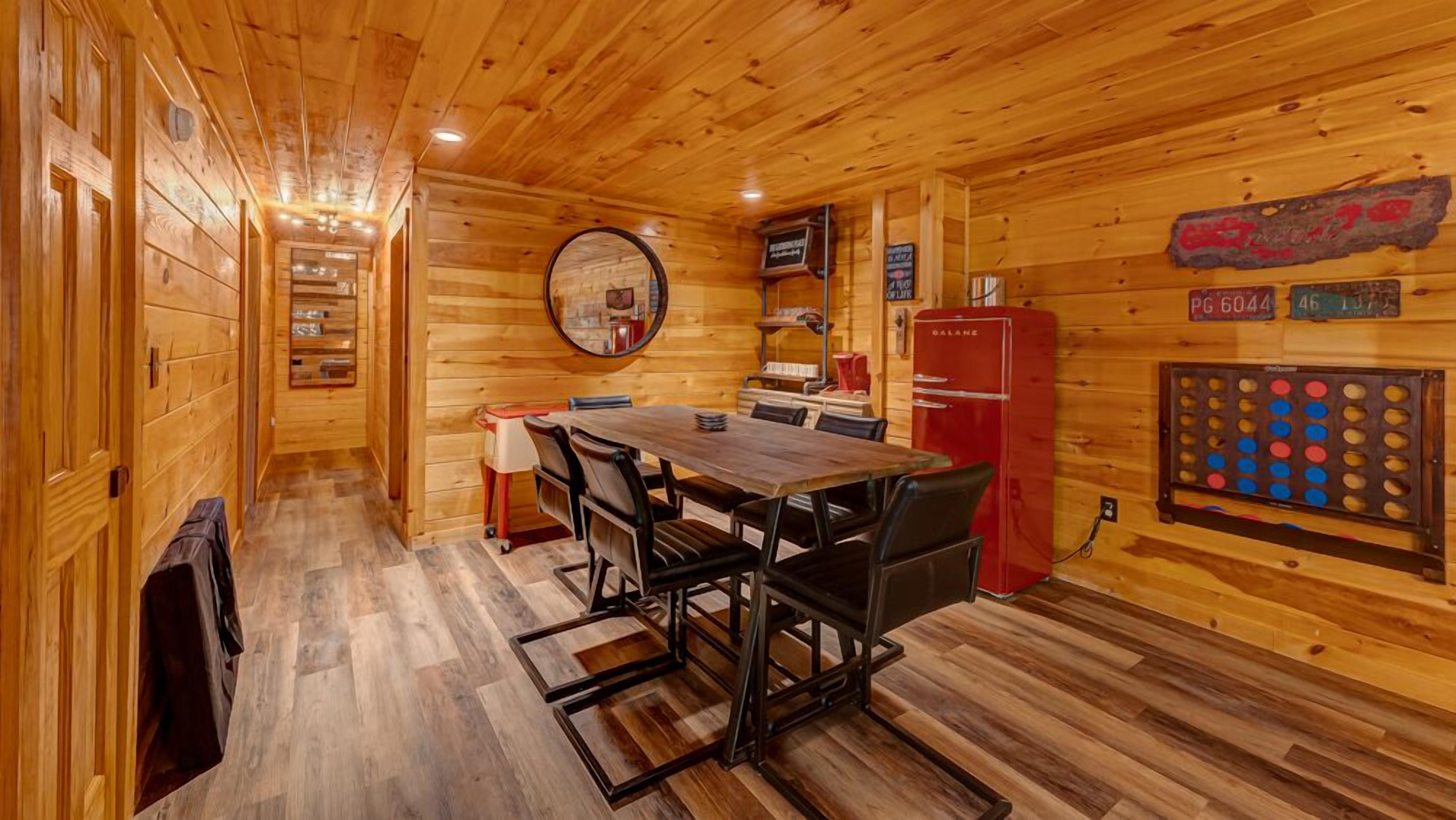 Ein Holzinterieur mit einem Esstisch, Stühlen, einem Kühlschrank und einer Dartscheibe.