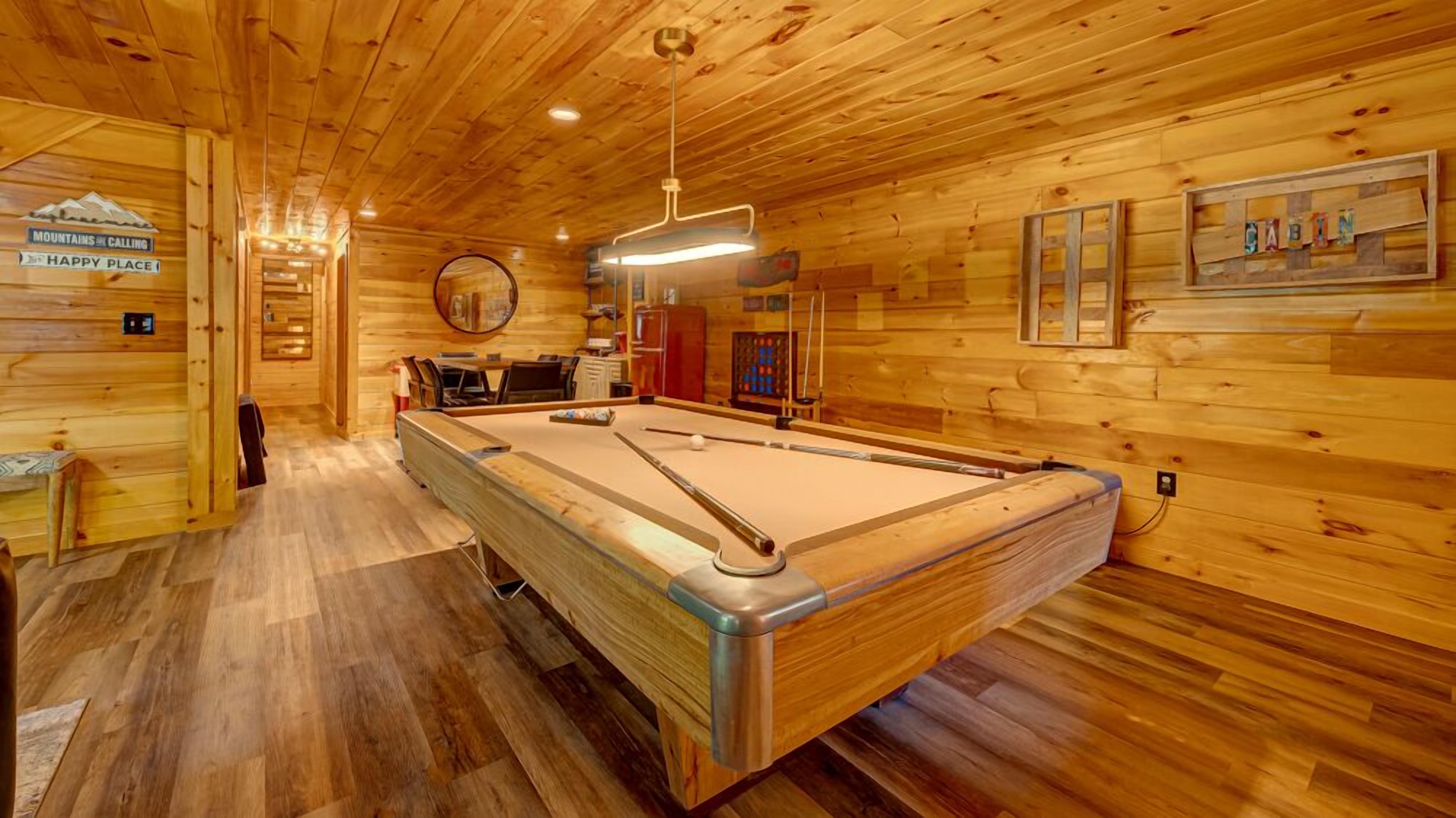 A pool table in a wooden room with a sign reading "Mountains Calling" and "Happy Place."