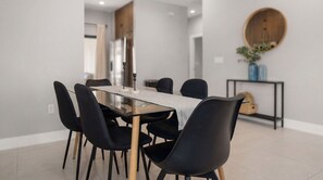 A modern dining area with a glass table, black chairs, and a wooden floor.