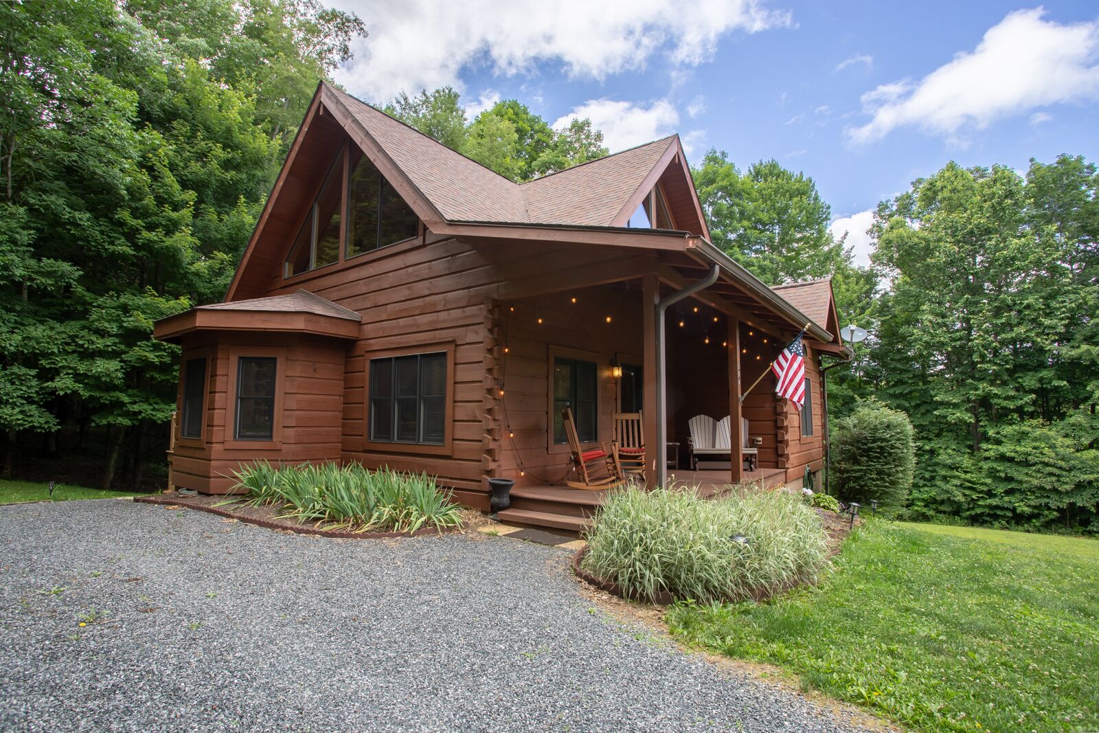 A log cabin with a porch, a flag, and a gravel driveway.