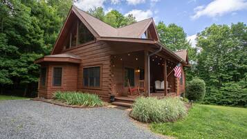 A log cabin with a porch, a flag, and a gravel driveway.