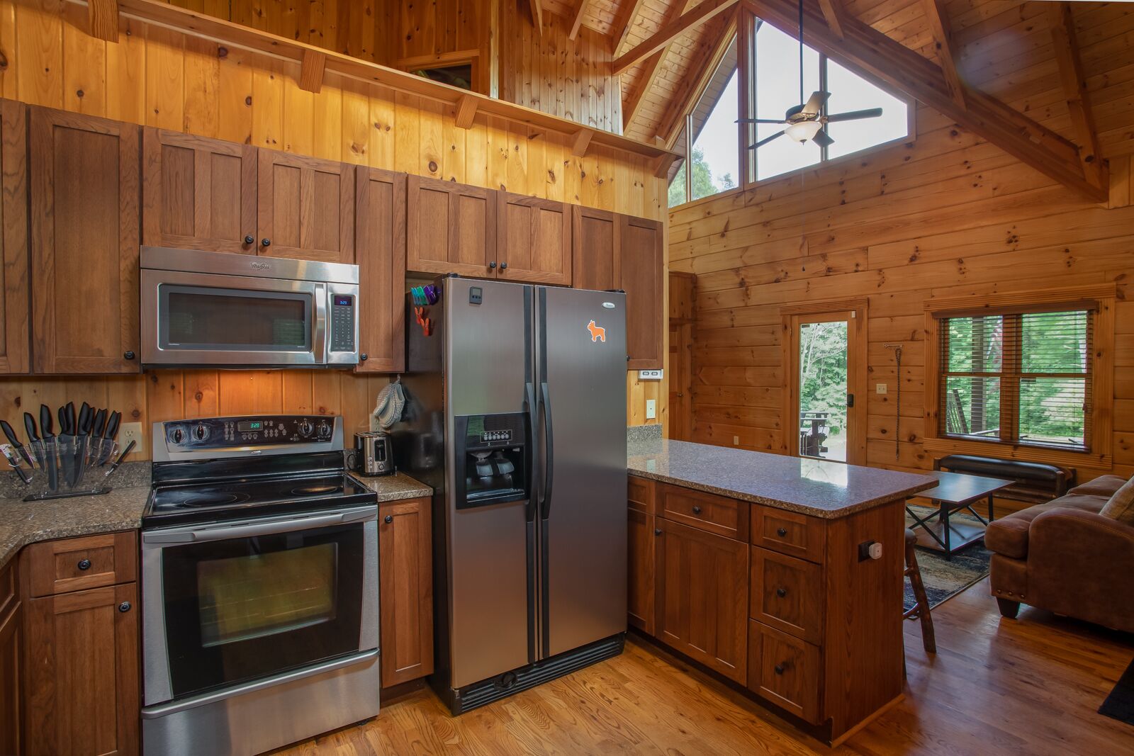A wooden cabin kitchen with a stainless steel refrigerator, microwave, oven, and a coffee maker.