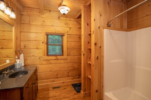 Baño de cabaña de madera con lavamanos, espejo, ventana y ducha.