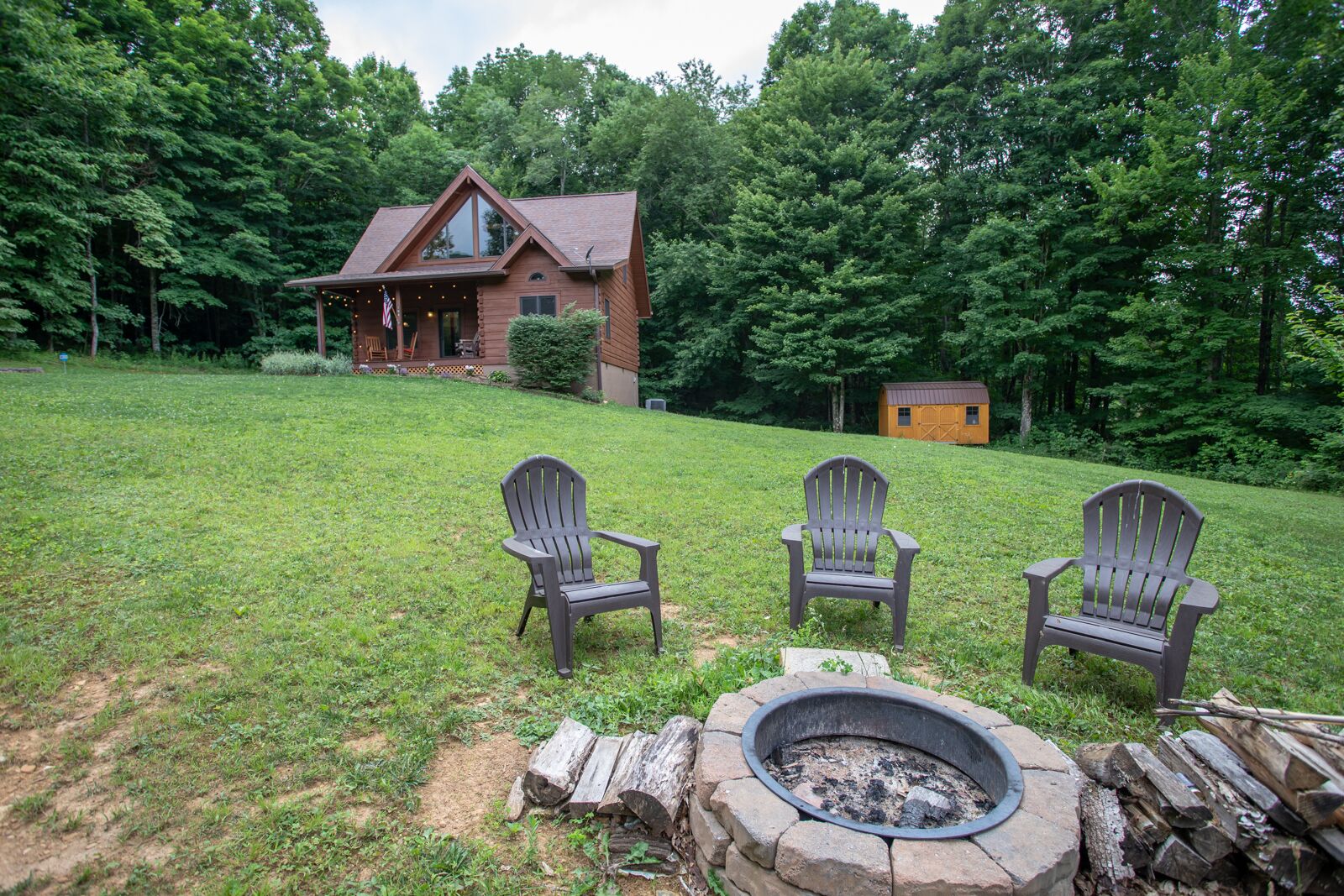 A cabin with a fire pit and two Adirondack chairs in the yard.