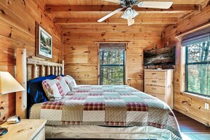 A wooden cabin bedroom with a bed, a dresser, a television, and a window with a view of trees. - Cute Cabin w/ hot tub, fire pit, pool table - close to PF/Gatlinburg! (Sevierville)