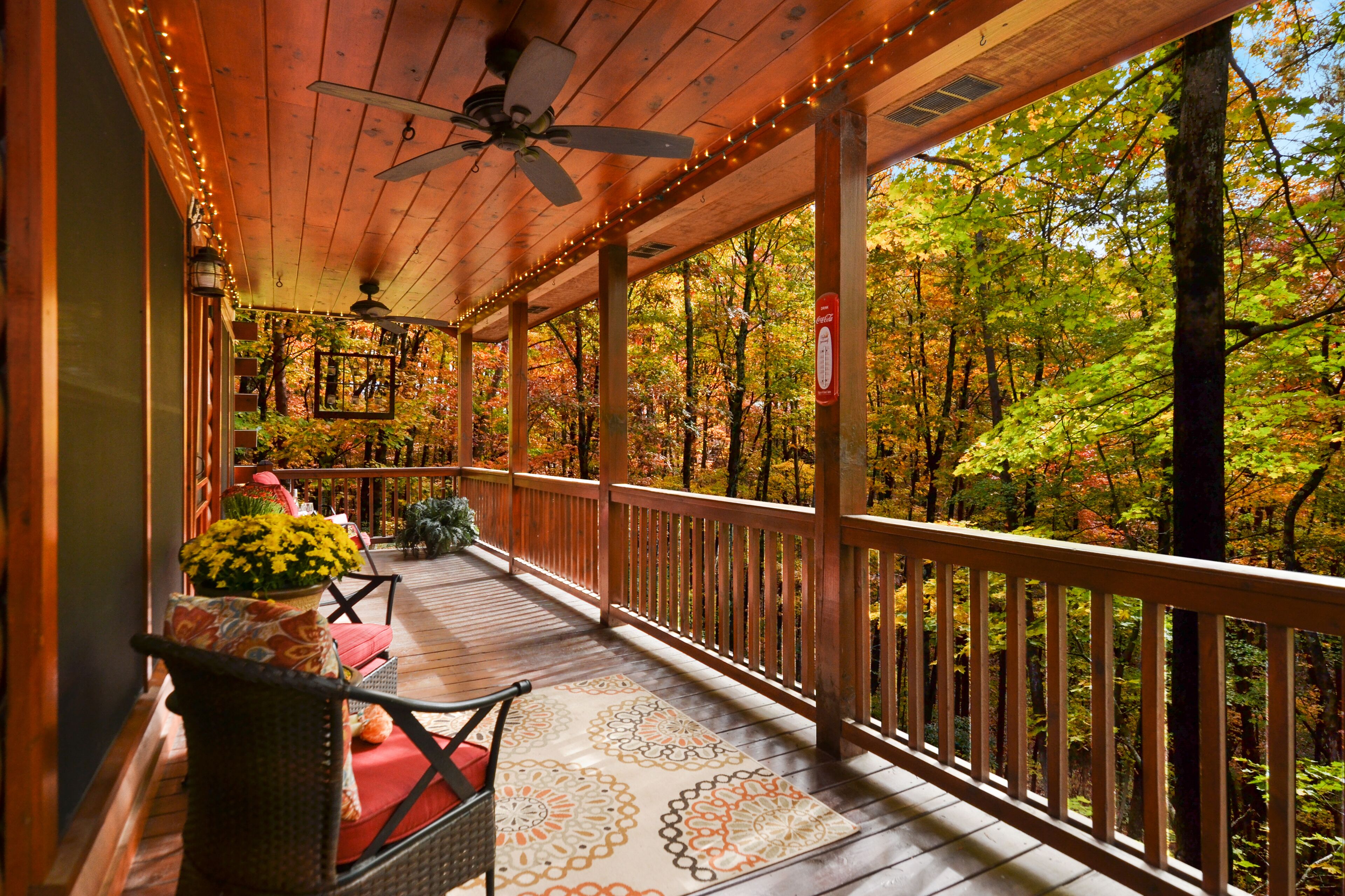 A covered porch with wooden railings, a ceiling fan, and string lights.